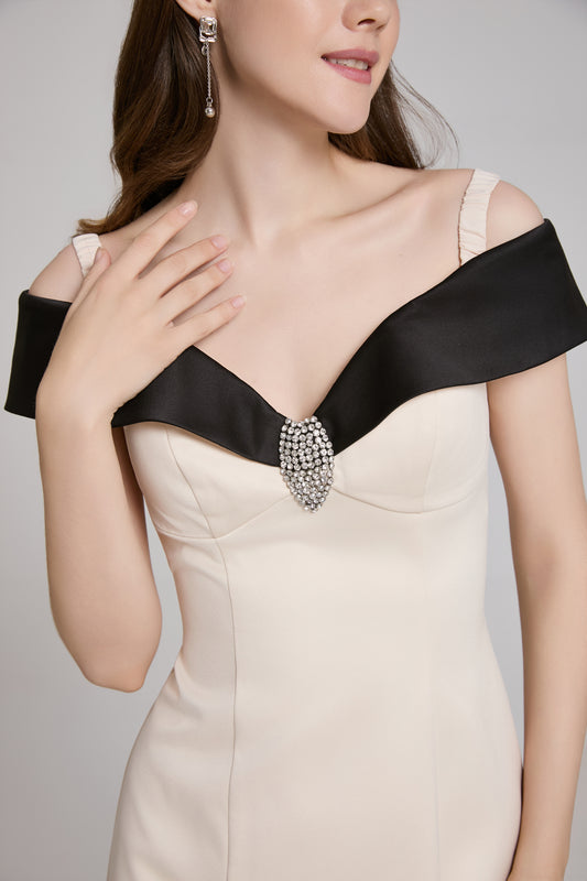 Woman wearing a beige dress with black accents and a decorative brooch on a plain background